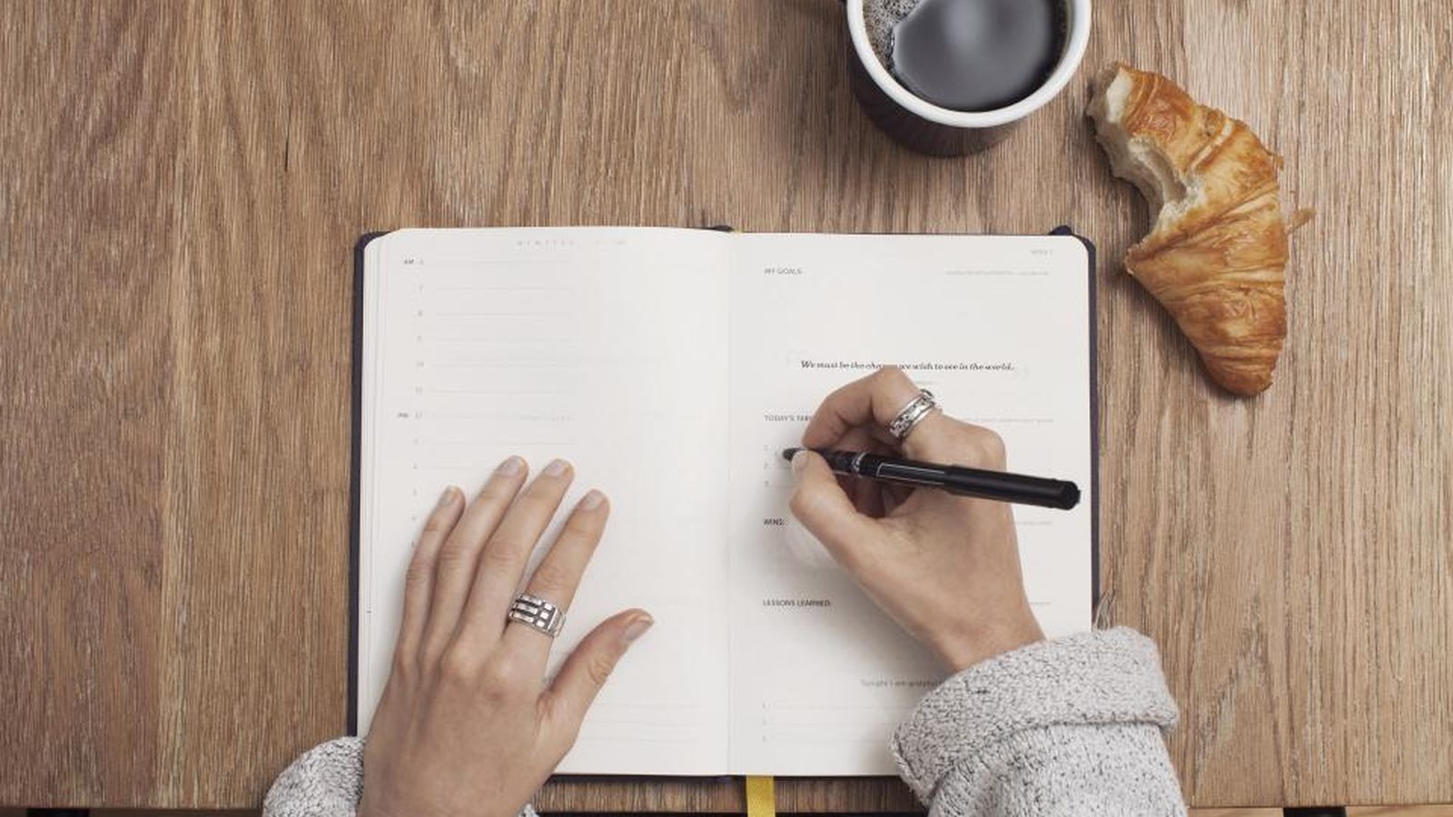 Hands writing goals in a journal beside a cup of coffee