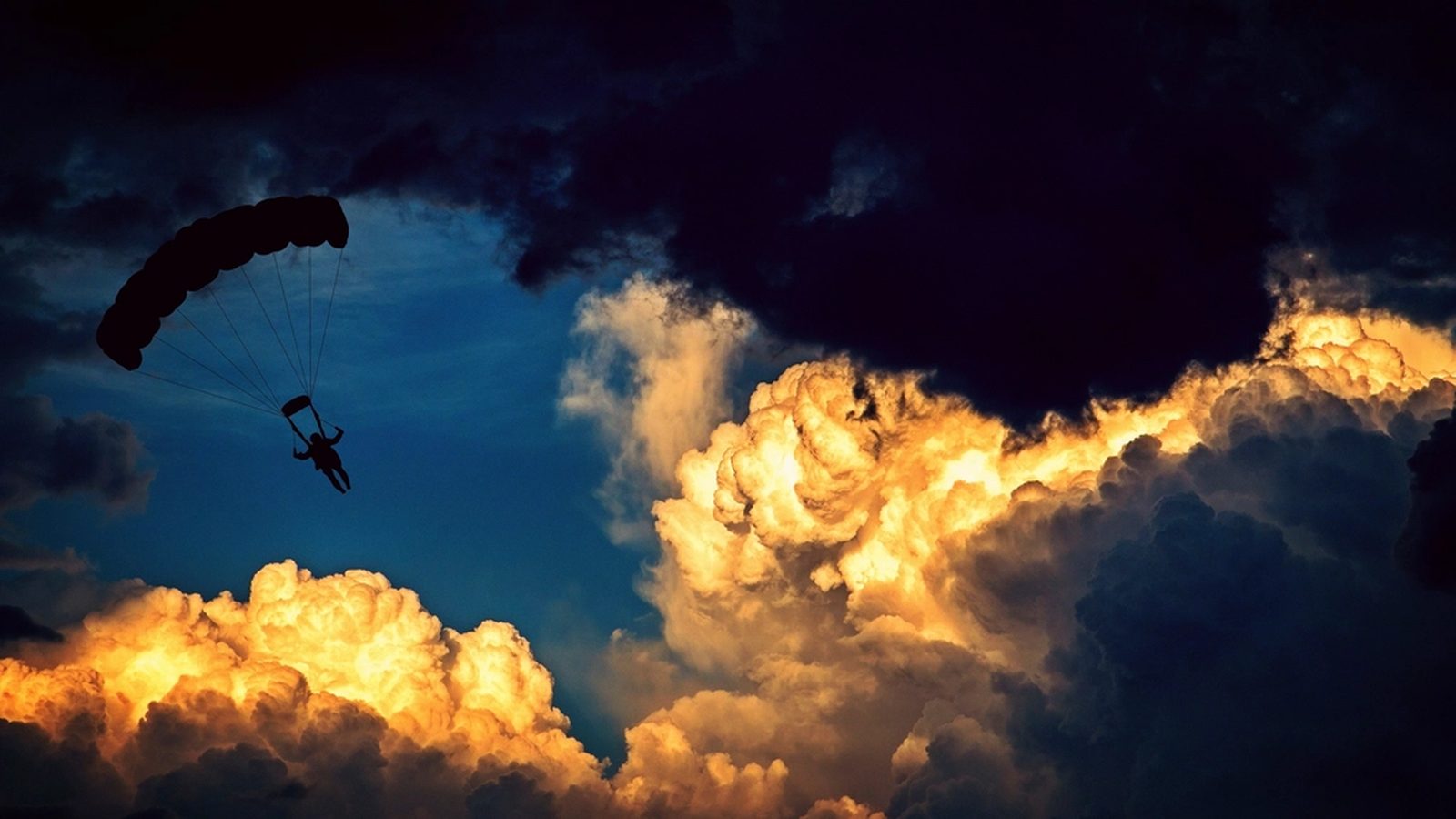 A skydiver under a parachute against golden sunset clouds