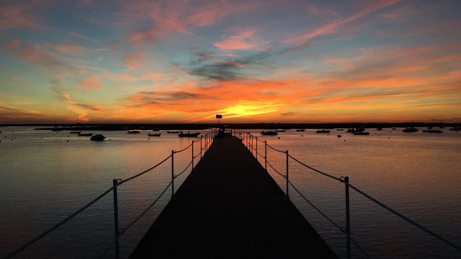 A pier stretching toward a vivid sunrise over calm water